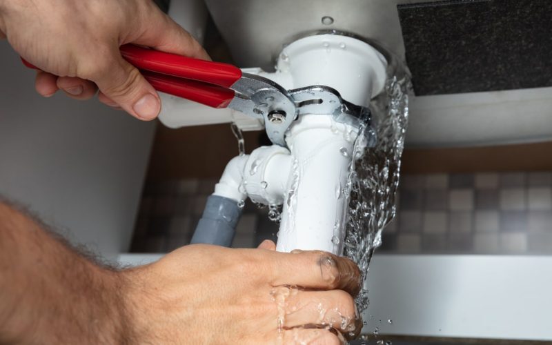 Close-up Of Male Plumber Fixing White Sink Pipe With Adjustable Wrench